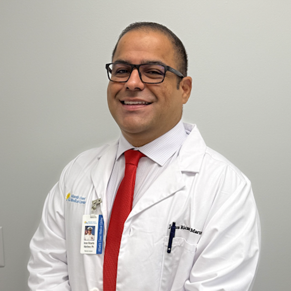 dr Jesus A smiling man in a white lab coat, red tie, and glasses stands against a plain light background.